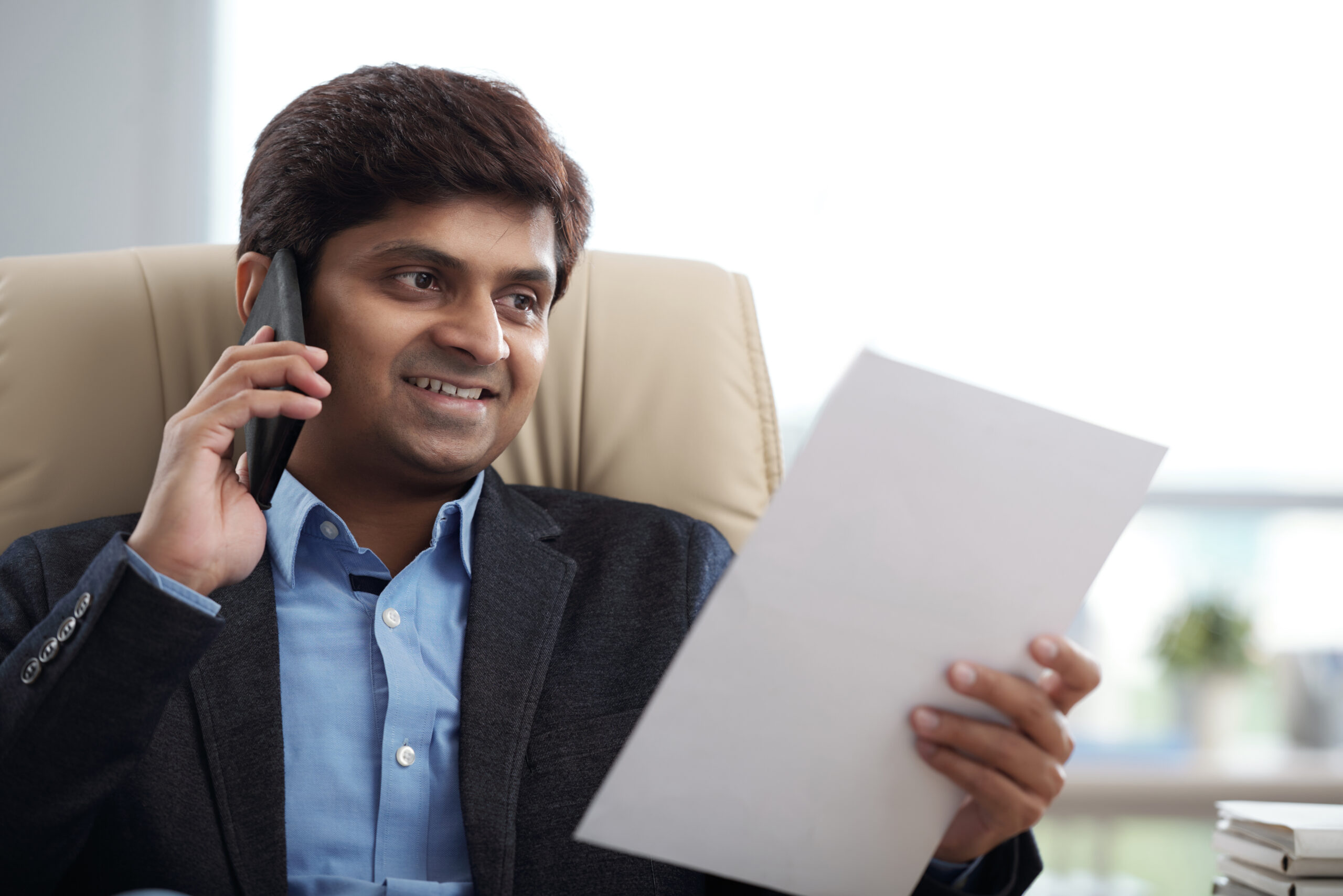 Smiling Indian entrepreneur talking on phones and reading business contract