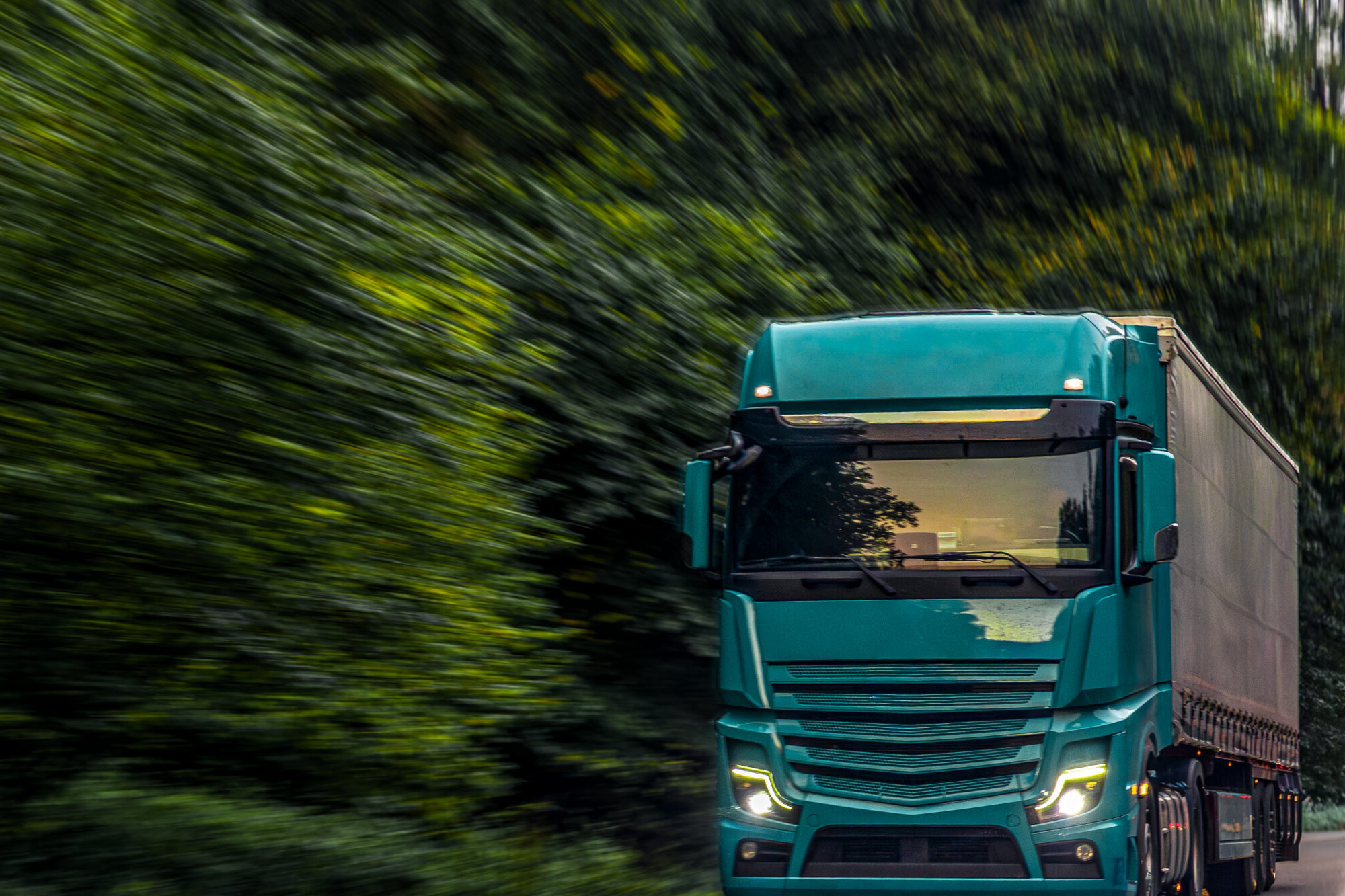 A powerful emerald green truck driving fast through a forest road, symbolizing innovation, energy, and modern logistics strength.